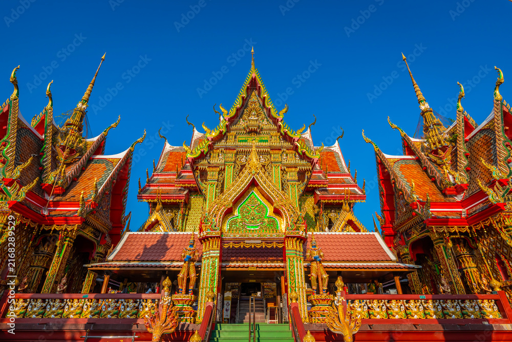 Fototapeta premium Intricate golden architecture of Wat Sri Uthumphon, a famous Buddhist temple in Mueang Nakhon Sawan District, Nakhon Sawan, Thailand, featuring ornate Thai artistic details under a bright clear blue s