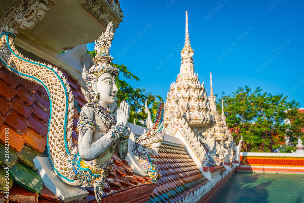 Fototapeta premium Detailed angel sculpture and Naga serpent roof decoration at Wat Sri Uthumphon in Mueang Nakhon Sawan District, Nakhon Sawan, Thailand, set against a clear blue sky background.