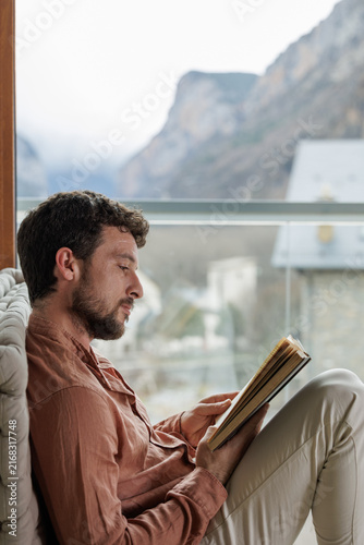 Young man reading a book by a window in a peaceful moment of learning and relaxation