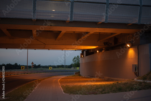 Urban concrete overpass above road and sidewalk, artificial light