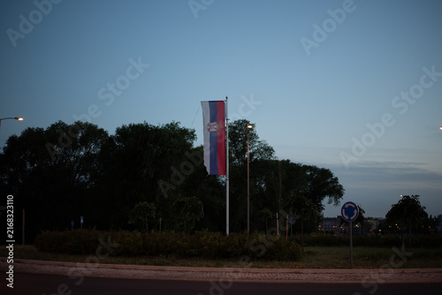 Flag of Serbia with national emblem on flagpole at twilight in Novi Sad