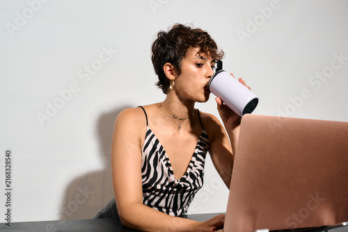 Businesswoman working at Office. DIrect flash shot. She sips from a mug while focused on her laptop, immersed in her tasks. 