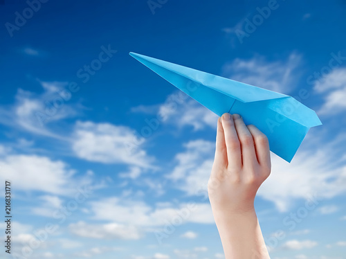 Hand holding a blue paper airplane against a bright sunny sky for travel and innovation