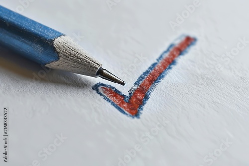 Pencil marking a red and blue checkmark on textured white paper