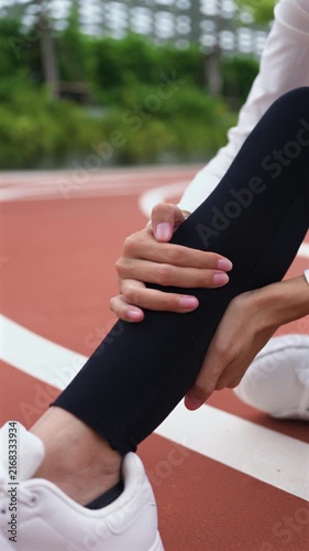 Close-up of Asian woman holding her painful calf on running track during workout. Calf muscle strain, leg cramp, runner injury, sports accident, and healthcare concept. Vertical Shot