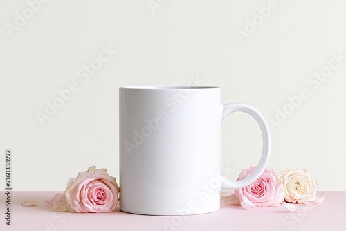 Blank white mug on pastel surface with delicate pink roses