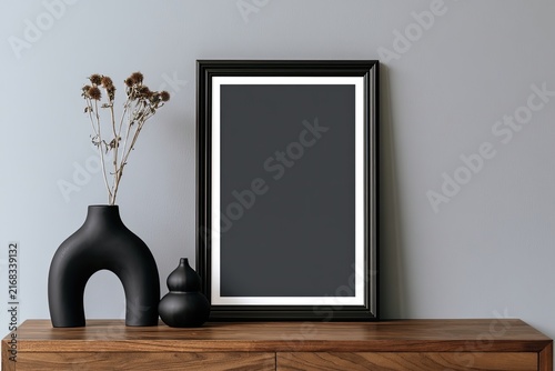 Minimalist black vase with dried plant beside black framed art on wood