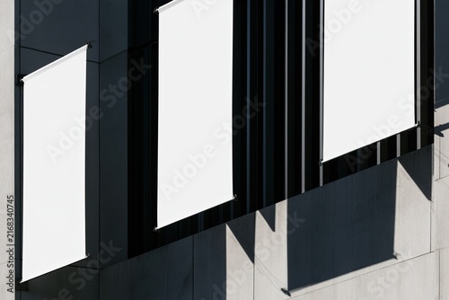 Four blank white banners hang from a modern building facade