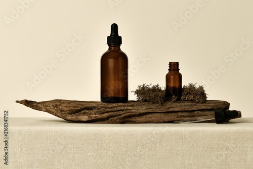 Two amber glass dropper bottles with organic elements on driftwood