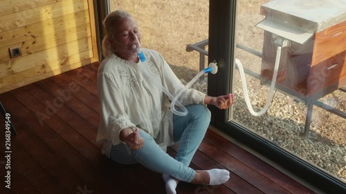 Mature woman in her performs breathing exercises and meditates calmly while using a mask for beehive air inhalation in an apitherapy chamber.