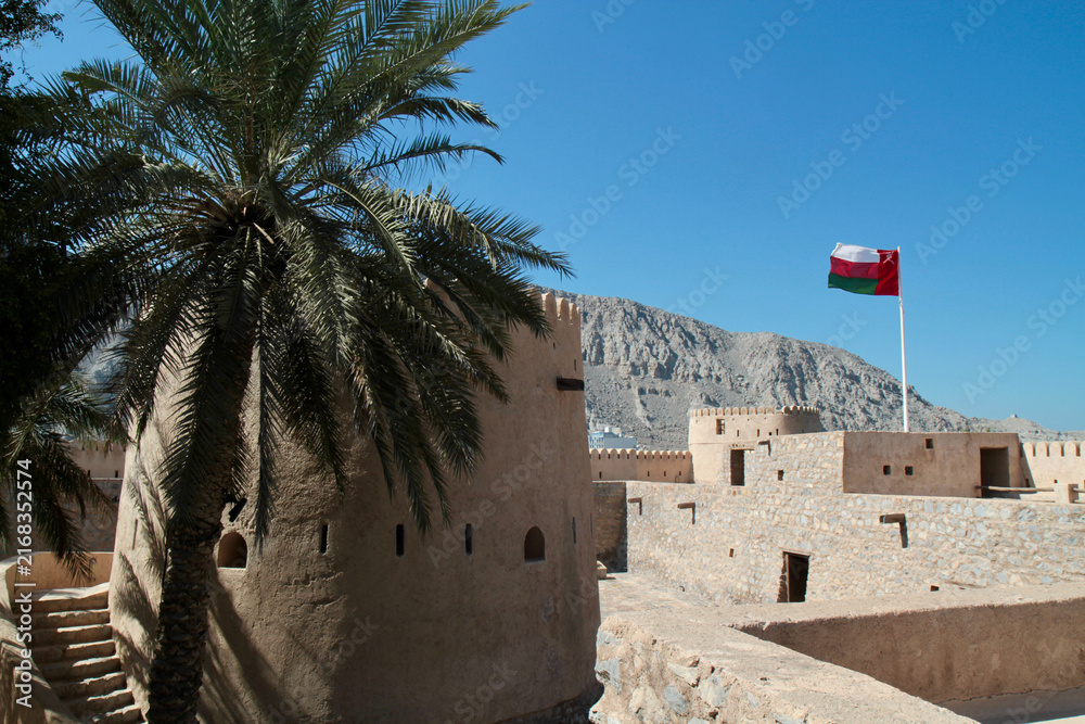 Naklejka premium Khasab Fort ramparts with Omani flag and palm tree, Musandam, Oman