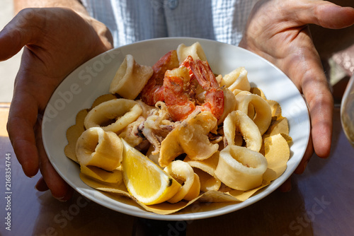 Italian mixed fried seafood served on a plate, featuring crispy fried calamari cuttlefish, and shrimp. Man hands holding Italian seafood dish.