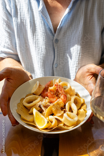 Italian mixed fried seafood served on a plate, featuring crispy fried calamari, cuttlefish, and shrimp. Man hands holding traditional Italian seafood dish, Mediterranean cuisine. Vertical image.