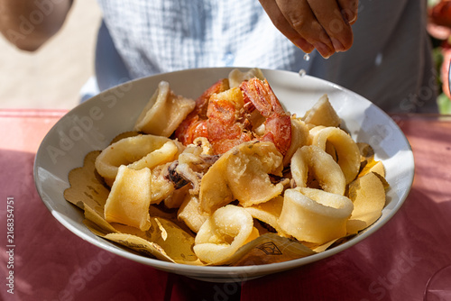 Italian mixed fried seafood served on a plate, featuring crispy fried calamari rings, small cuttlefish, and shrimp. Man hand squeezing lemon, rustic food styling and authentic Mediterranean cuisine.