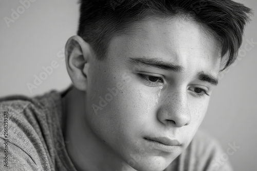 young man sits with his head bowed tears streaming down his cheeks immersed in memories of joyful childhood