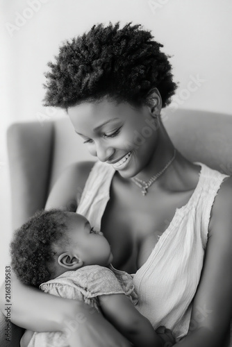warm tender moment captured as mother gently rocks her darkskinned infant in cozy chair by window