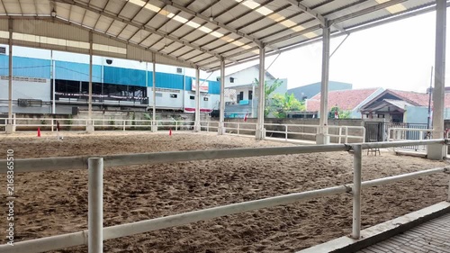 Covered horse riding arena with dirt floor and white fences.