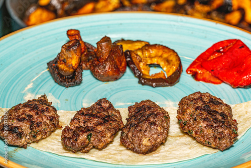 Traditional grilled Turkish köfte meatballs served hot on a plate with grilled peppers, onions, and fresh parsley. Authentic Middle Eastern cuisine.