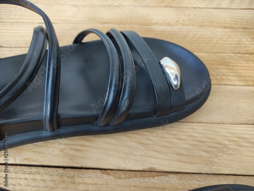 Close up of black sandal straps with silver metal ornament on wooden surface