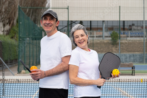 Smiling senior couple holding paddles and ball on a pickleball court