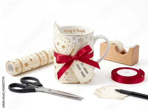 Christmas gift mug wrapped in gold star paper with red ribbon and gift tag on white