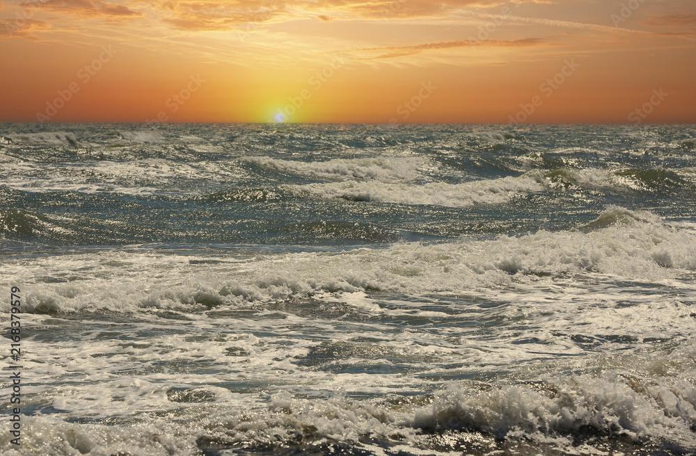 Obraz premium Golden sunset over a choppy ocean with waves crashing and foam