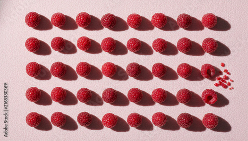 Raspberries arranged in a grid pattern on a pink surface