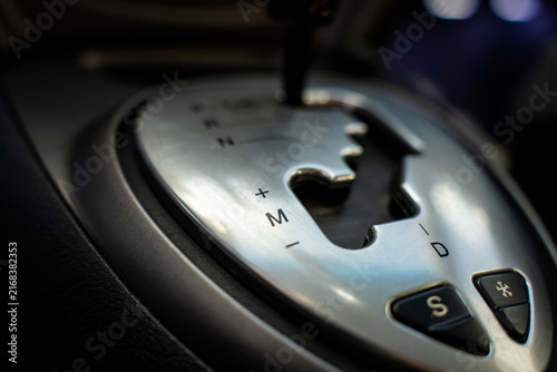 Automatic transmission gear shift lever on center console of modern car interior, close-up view of silver shifter plate and letters.