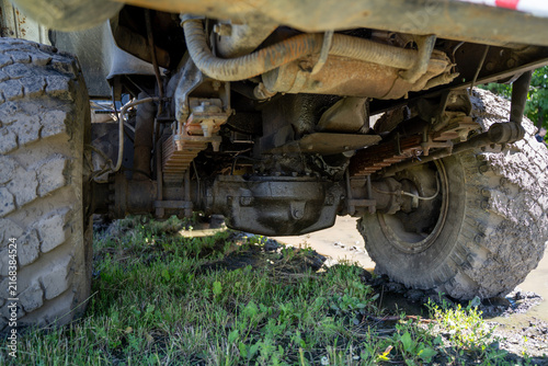 Quadro su tela Undercarriage view of heavy truck with dirty axle, leaf spring suspension, and muddy wheels on off-road terrain during daytime