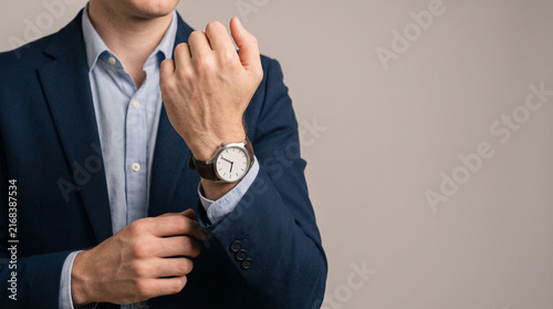 Business executive in navy suit adjusting sleeve cuff while checking classic watch, close up mid shot. Time management, punctuality, corporate scheduling and productivity concept.