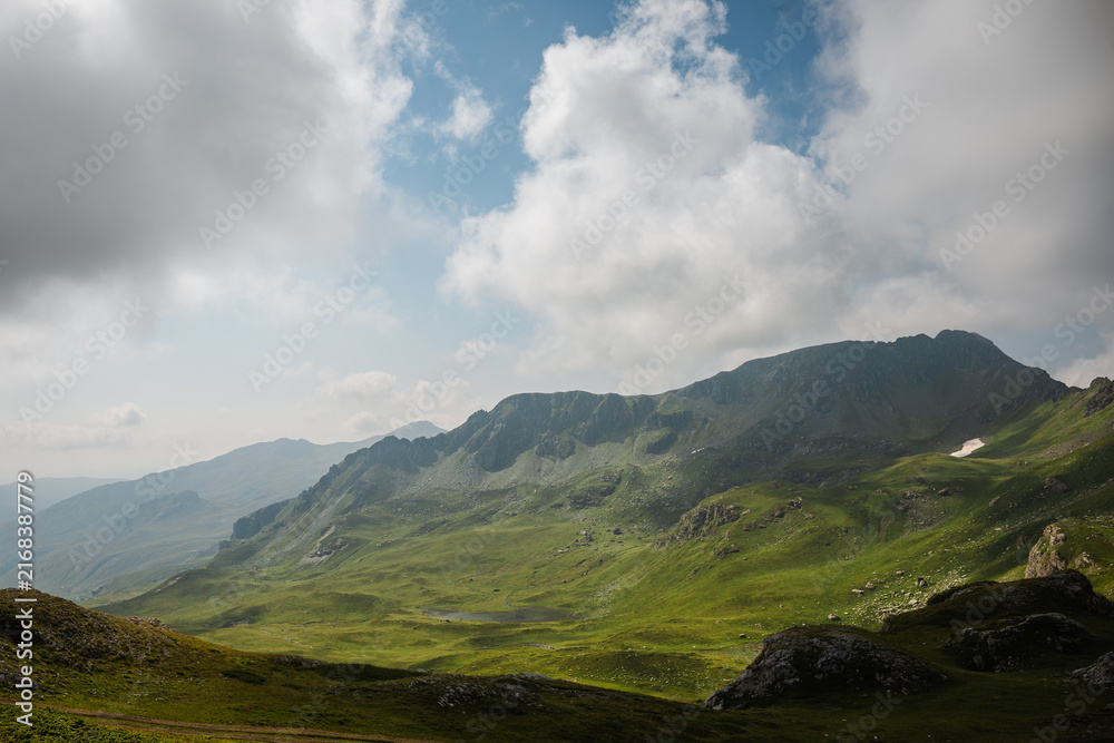 Fototapeta premium Green mountain ridge beneath dramatic white clouds and blue sky
