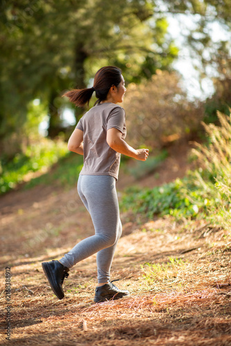 Obraz na plátně Asian woman running uphill on forest trail during outdoor workout