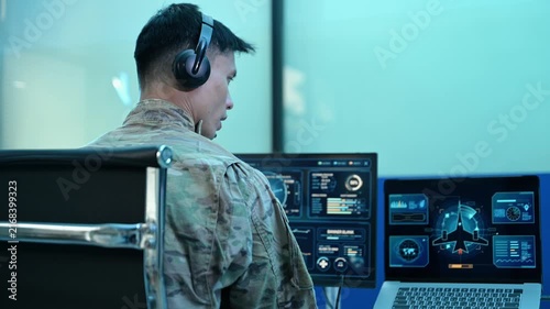 Military operator with headset analyzes radar HUD screens and takes notes in high tech command center, ensuring strategic cyber