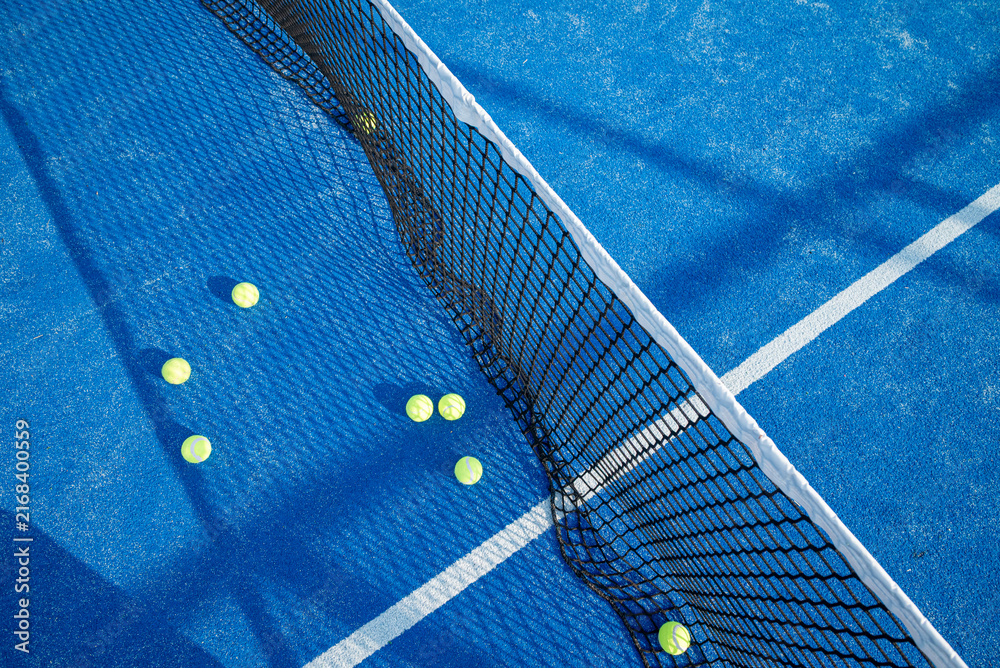 Fototapeta premium Aerial top down view of a black tennis net and yellow balls scattered on a vibrant blue artificial turf court