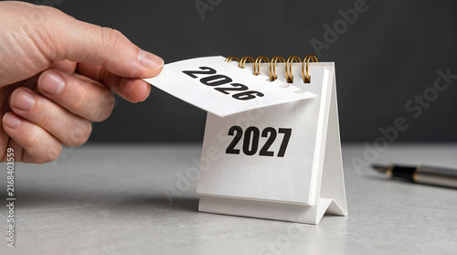 Hand Flipping Desk Calendar Page from 2026 to 2027 on Office Desk