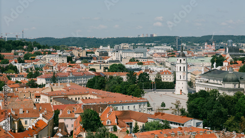 Aerial view of Vilnius old town bell tower rising above red rooftops with lush greenery nearby, lithuania tourism content, church landmark photography, city guide marketing, travel blog imagery