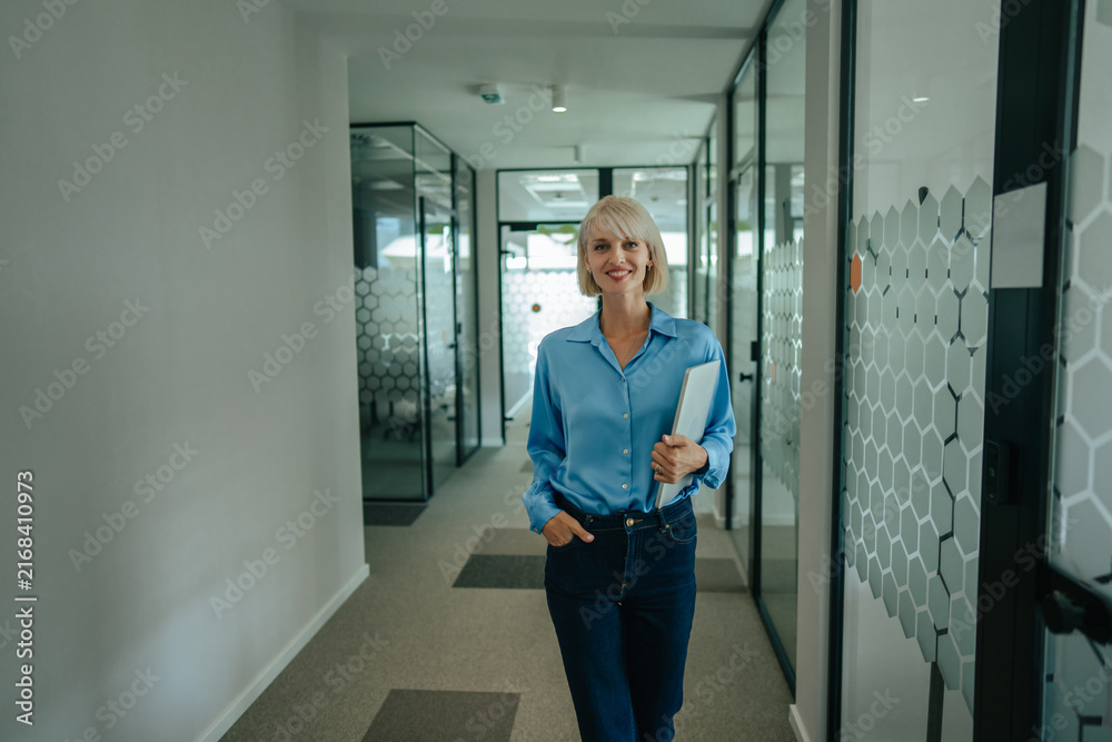 Fototapeta premium Businesswoman walking in modern office corridor holding laptop