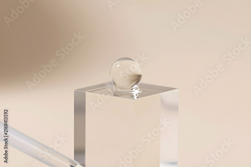 Extreme close-up of a drop of clear cosmetic serum on the edge of a clear acrylic block.