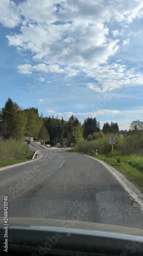 POV car driving on rural asphalt road approaching road work and speed limit sign in green mountain landscape, dashcam point of view journey on countryside highway under blue cloudy sky