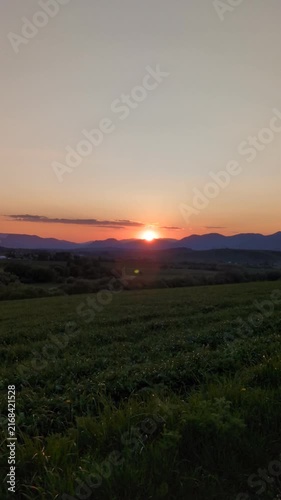 Scenic golden sunset over mountain ridge and green meadow landscape, peaceful evening horizon with orange sky during twilight countryside road trip journey in summer nature background view