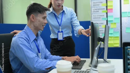 Two Asian software developers collaborating, discussing source code on screen, and troubleshooting