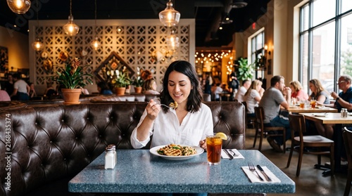 A woman eating a meal at a restaurant table with a drink and a cozy interior background