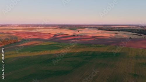 Aerial drone footage flying over picturesque rolling hills and cultivated farmlands, with beautiful long shadows stretching across the rural landscape during a warm and colorful sunset