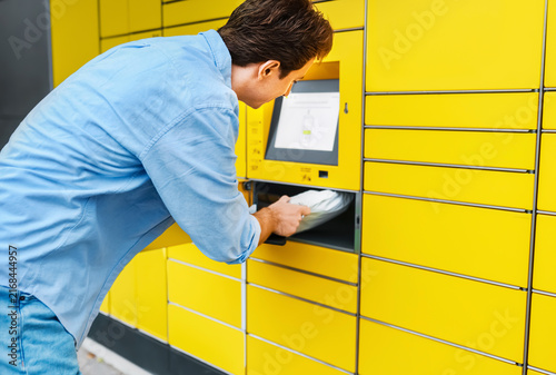 Foto man is receiving a package from a yellow automated parcel locker