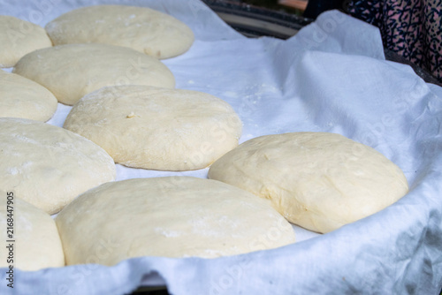 Fresh bread dough balls resting on a white cloth inside a tray. Traditional homemade raw yeast dough balls prepared for baking in a rural outdoor setting.