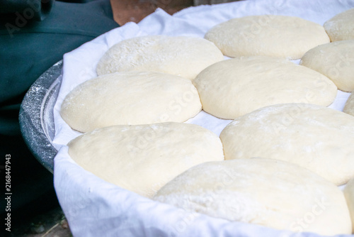 Fresh bread dough balls resting on a white cloth inside a tray. Traditional homemade raw yeast dough balls prepared for baking in a rural outdoor setting.