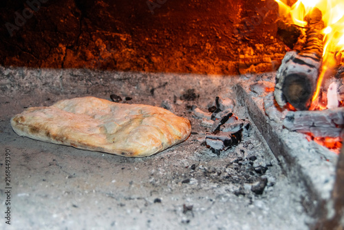 Traditional bread baking inside a rustic wood-fired barrel oven next to burning logs and hot embers. Authentic outdoor baking process in a rural village setting.