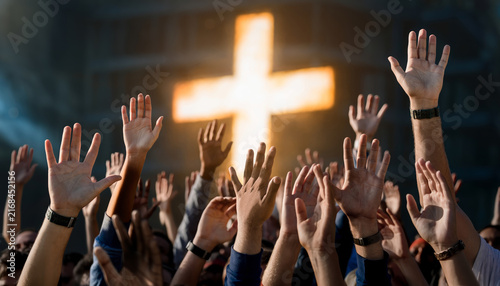 Group worshiping with hands raised towards glowing cross