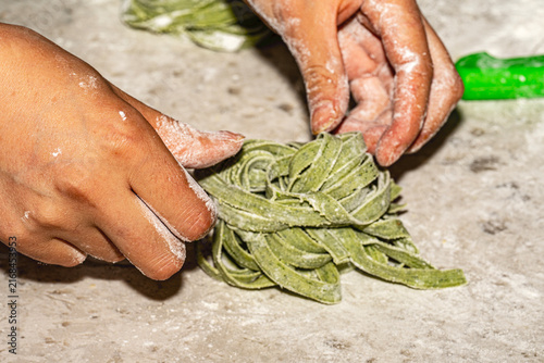 Freshly made artisanal tagliatelle pasta nests dusted with flour on a rustic wooden board. Raw homemade Italian fettuccine.