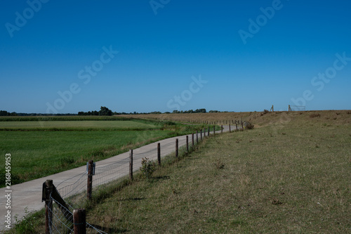 Photography A rural dike path leads along a fence under a clear blue sky, dike landscape on